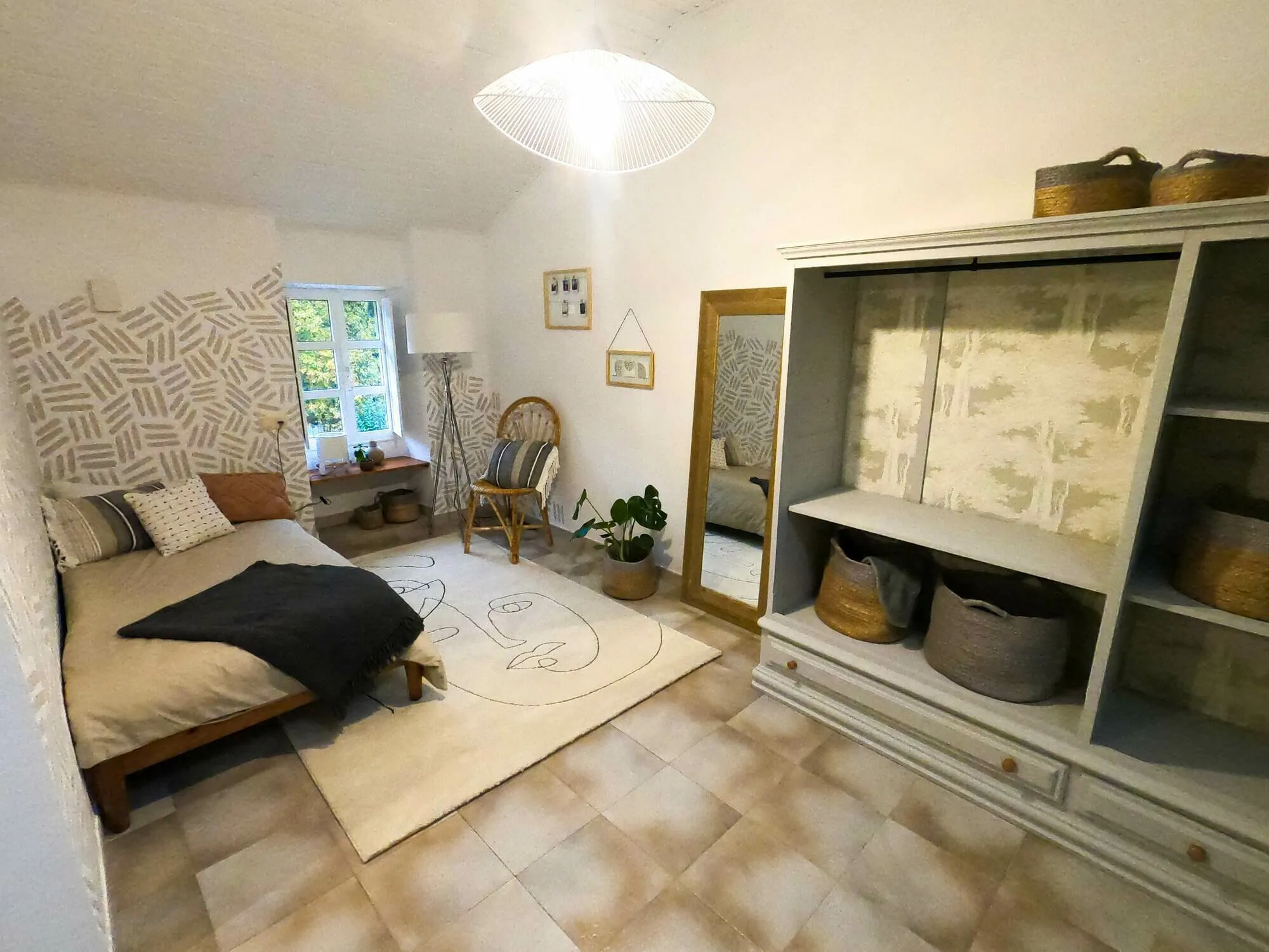 Room 104 after its redesign: a double bed against a hand-painted patterned wall, a full-length mirror, woven baskets and a plant