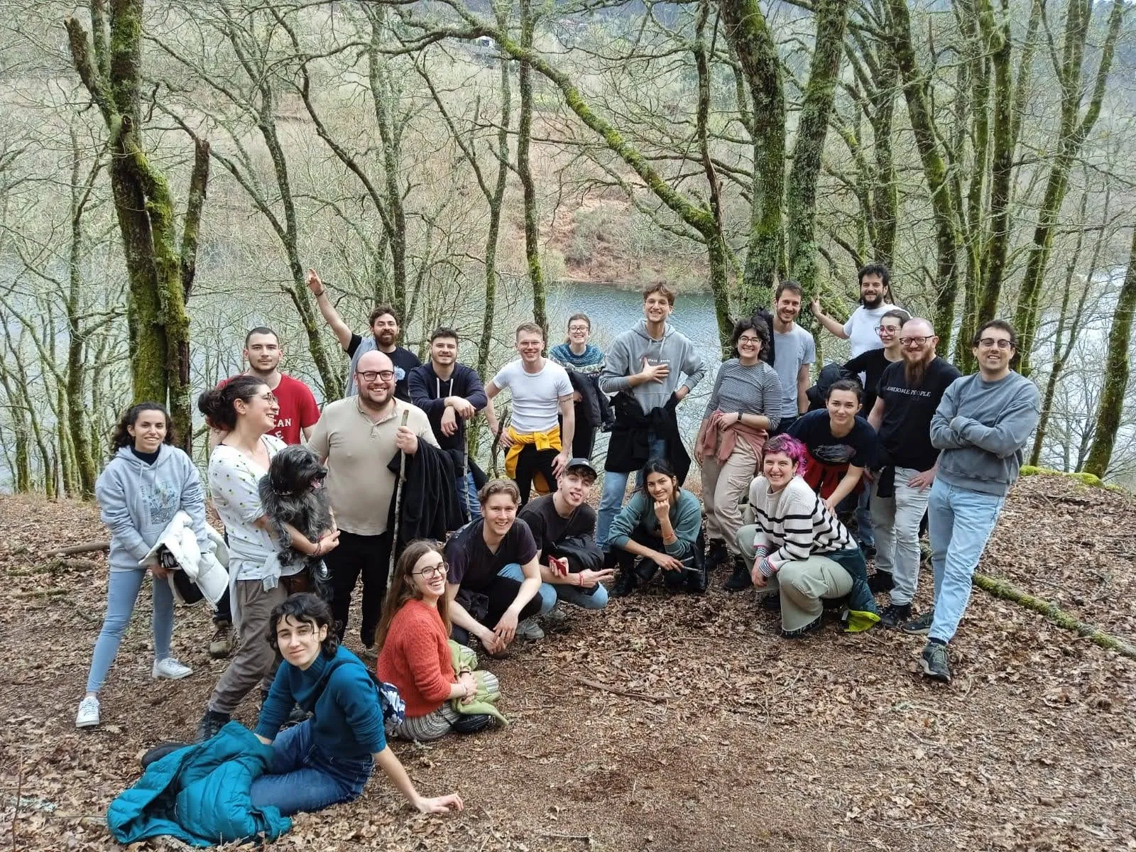 A group of about thirty people posing on a leafy hillside above a reservoir among bare trees