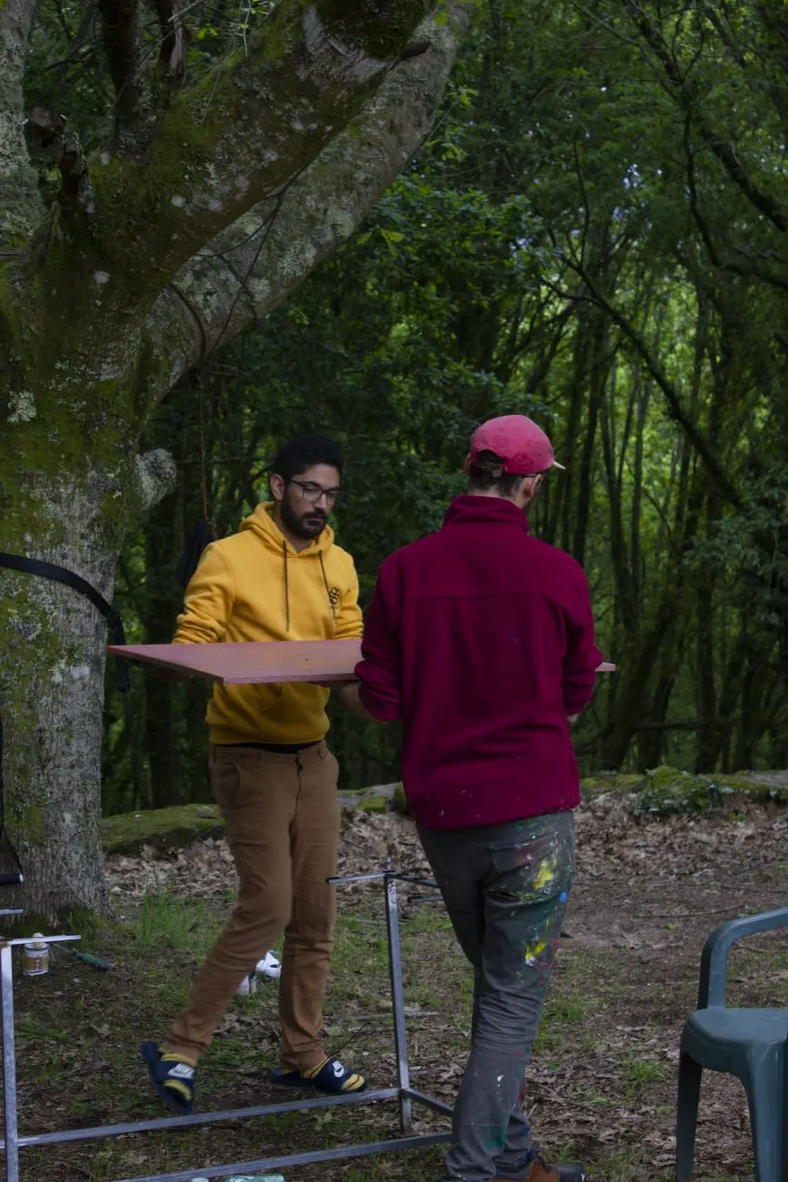 Two people carrying a freshly varnished wooden tabletop between them in a mossy oak wood
