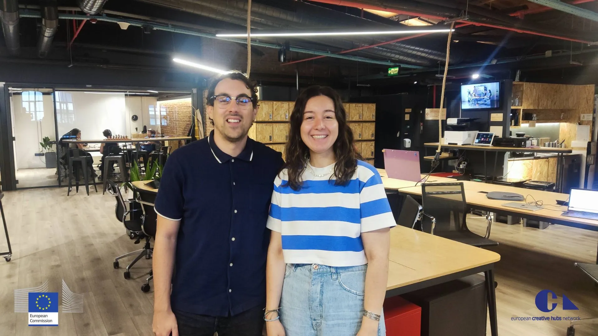 A man and a woman smiling in an open-plan coworking space, with European Commission and European Creative Hubs Network logos