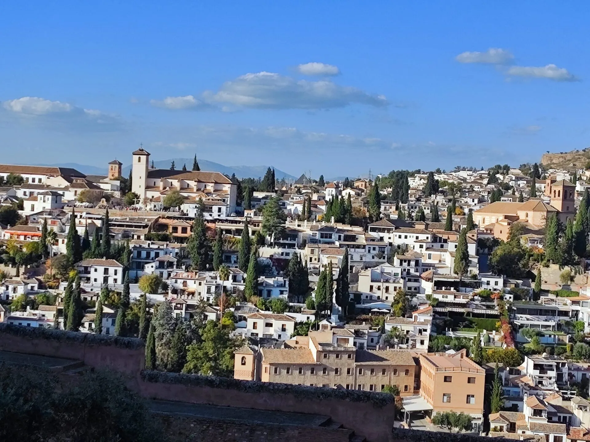 View across a hillside of whitewashed houses, cypresses and a church tower in Granada’s Albaicín