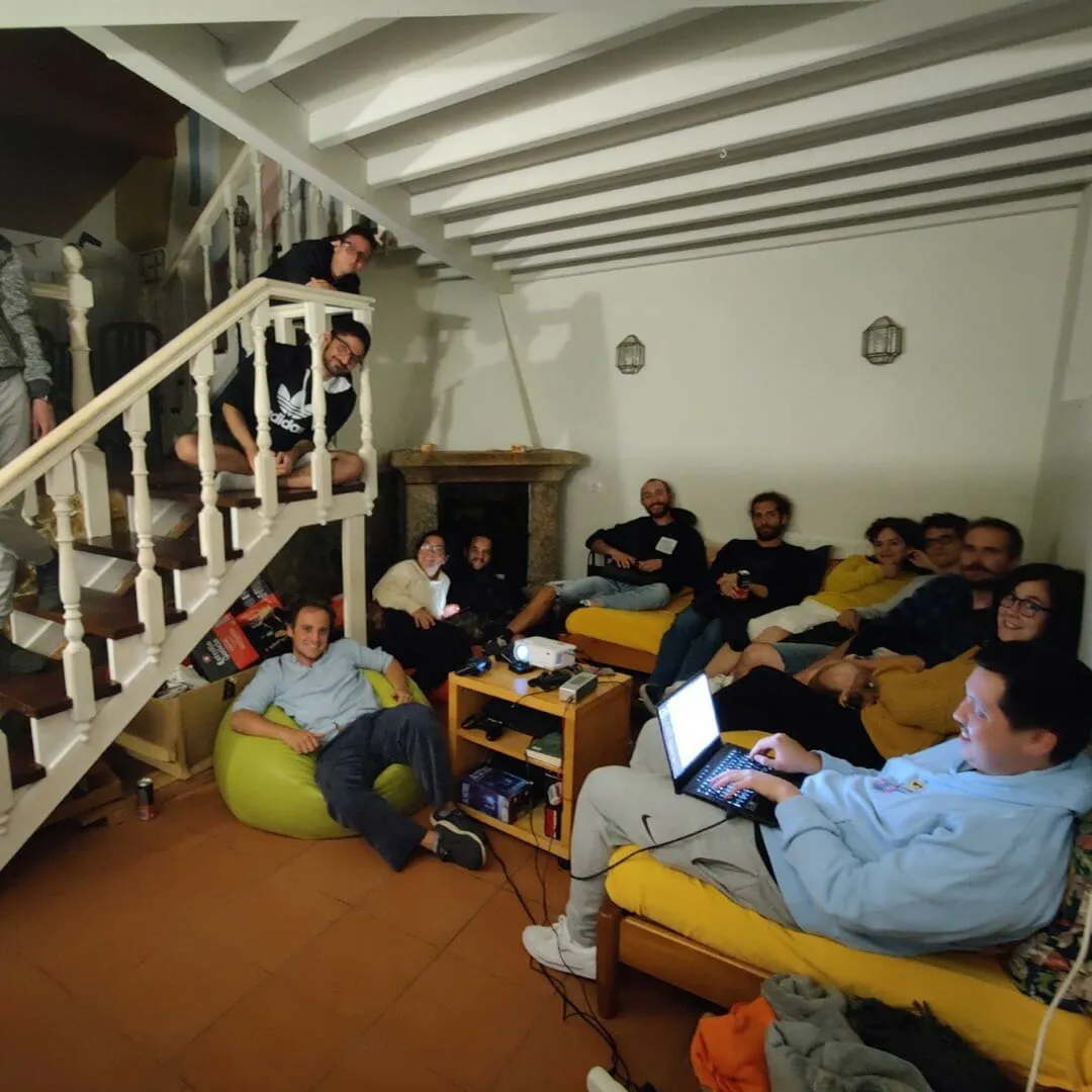 A dozen colivers gathered in the living room around a projector, spread across sofas, a bean bag and the stairs