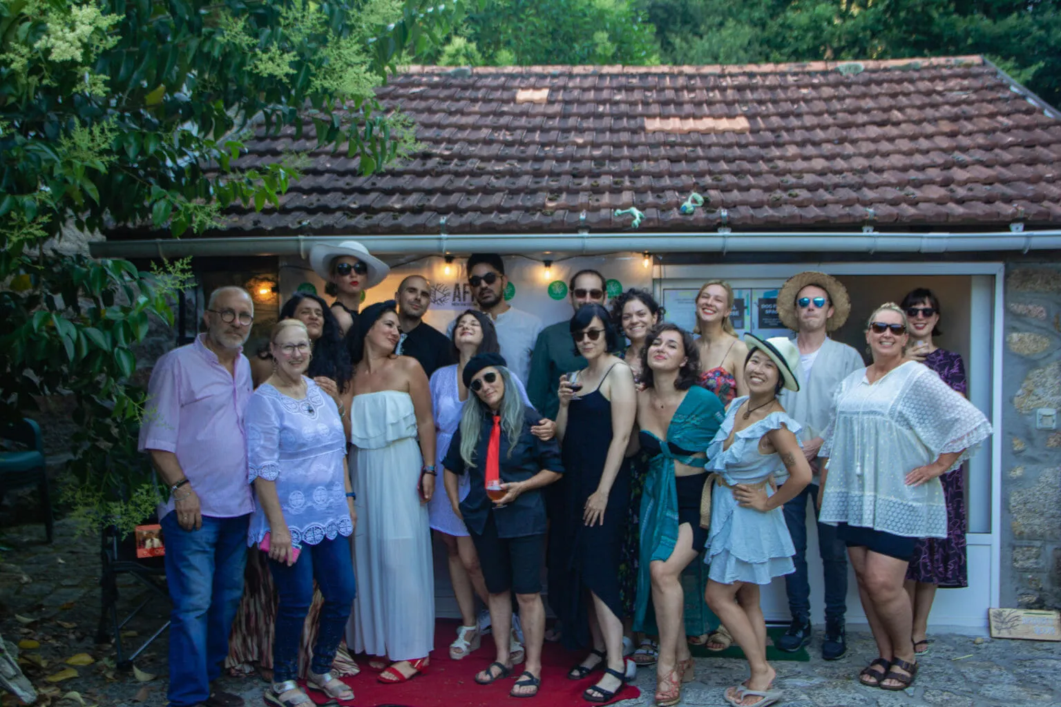 Some twenty people dressed up on a red carpet outside a tiled-roof building hung with festival lights