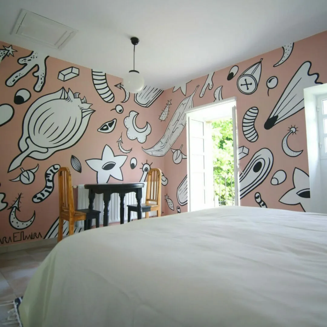 Bedroom with pink walls covered in black-and-white doodle murals, a wide white bed and a door open onto greenery