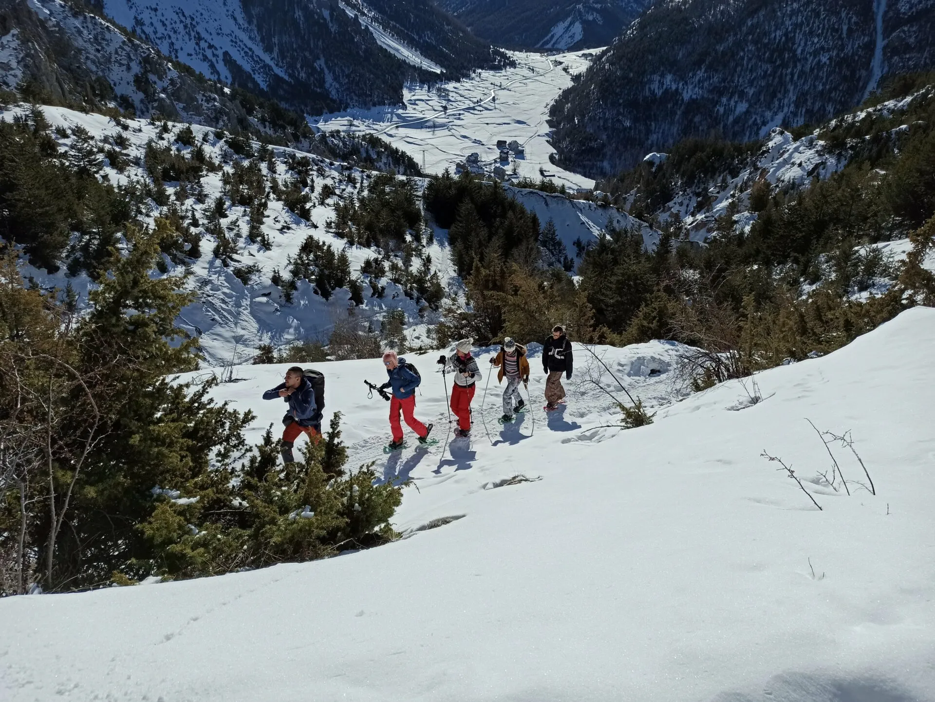 Five people snowshoeing along a snowy slope high above an alpine valley at Cloud Citadel