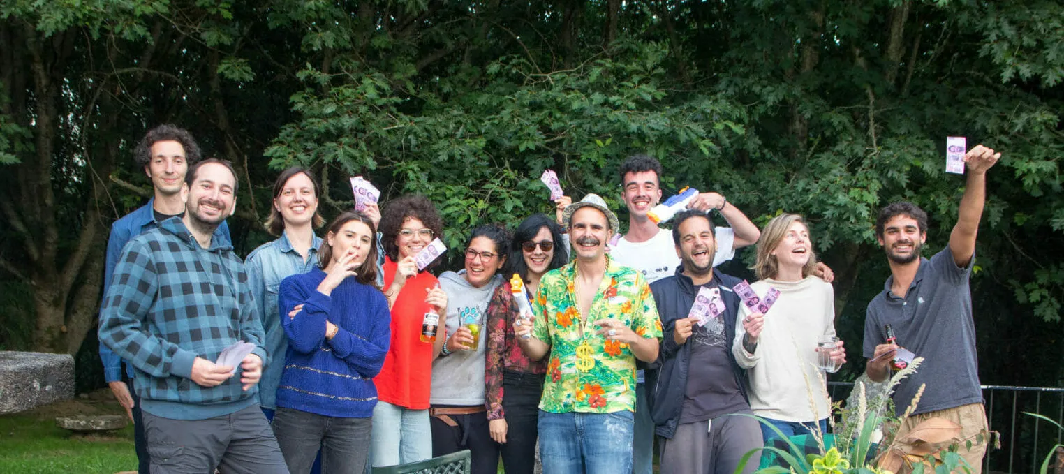 Thirteen laughing people in a garden holding small cards up to the camera