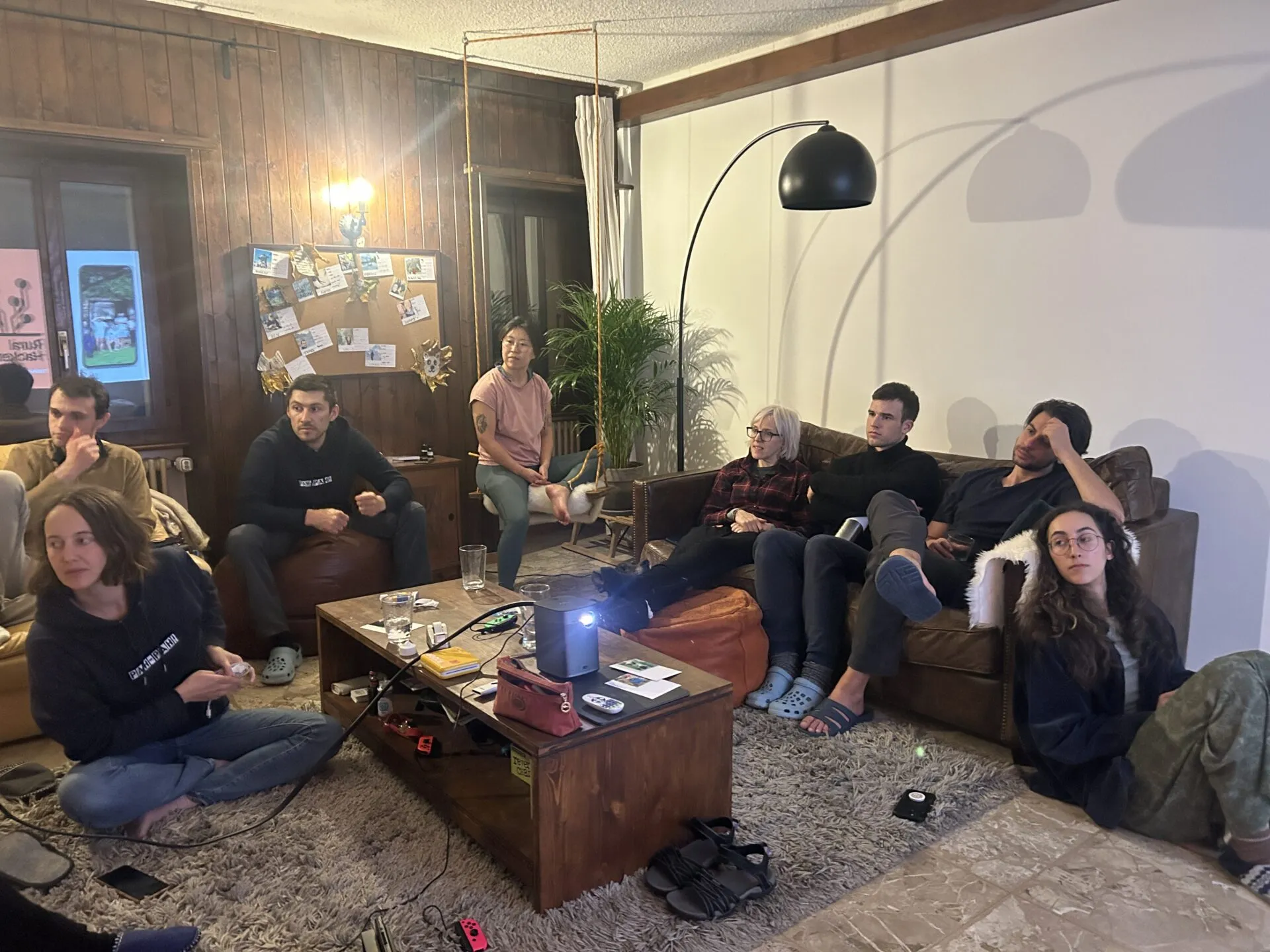 People relaxing on sofas and the floor of a wood-panelled living room, watching a projector on the coffee table