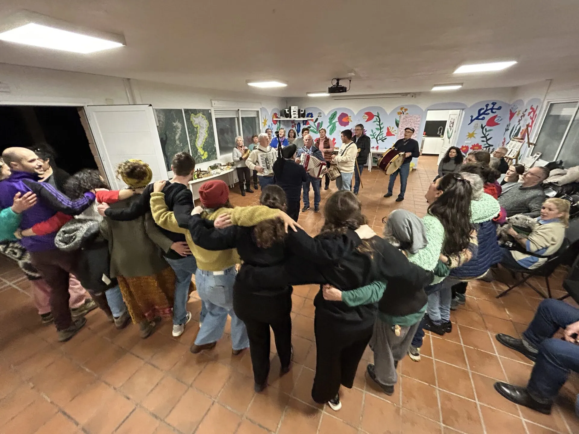 A big circle of people dancing arm in arm at the Casa do Pobo while the village band plays accordions and drums at the far end