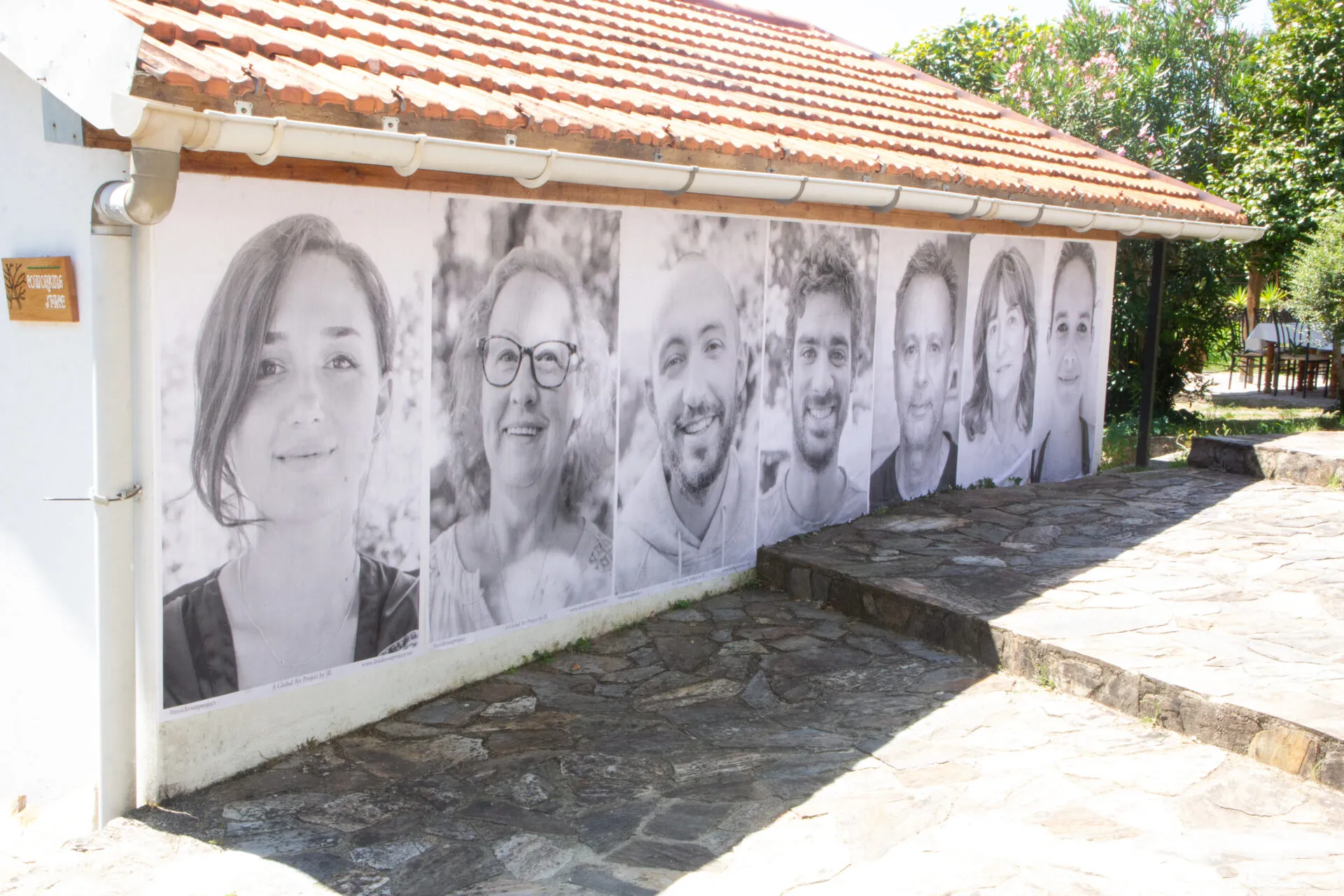 A row of large black-and-white portrait photographs pasted on the outside wall of a small tiled-roof building