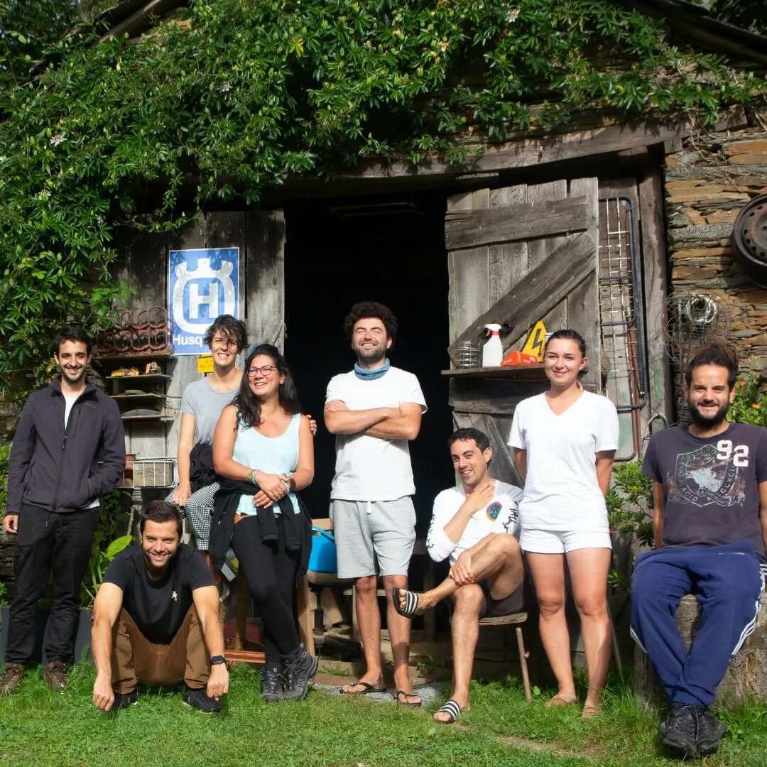 Ten people posing on grass in front of a vine-covered stone shed with an open wooden door