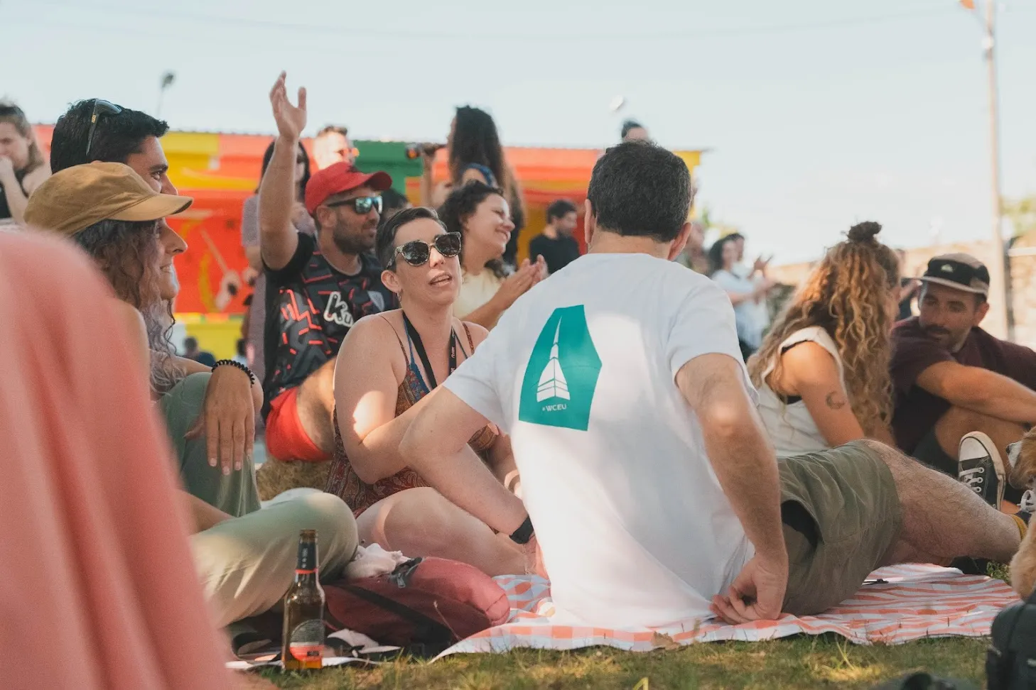 Gente sentada en mantas sobre la hierba en el Rural Hackers Fest, delante de un fondo pintado