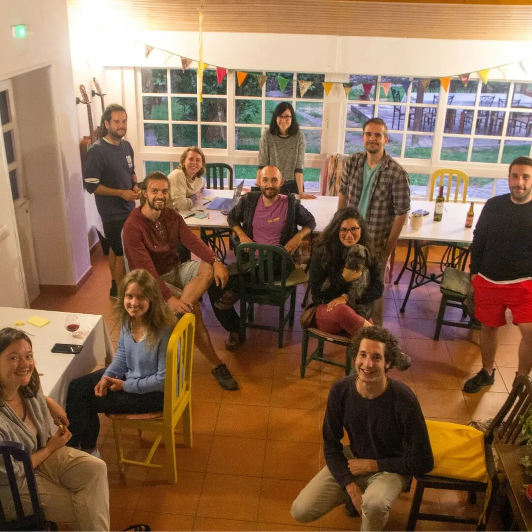 About a dozen people on mismatched chairs in a bright hall strung with bunting, looking up at the camera
