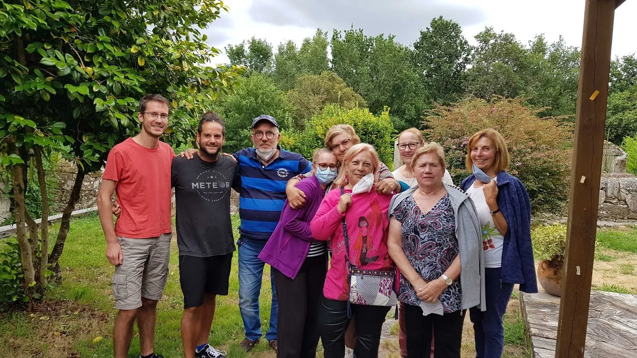 Two young men posing in a garden with a group of older women, some of them wearing face masks