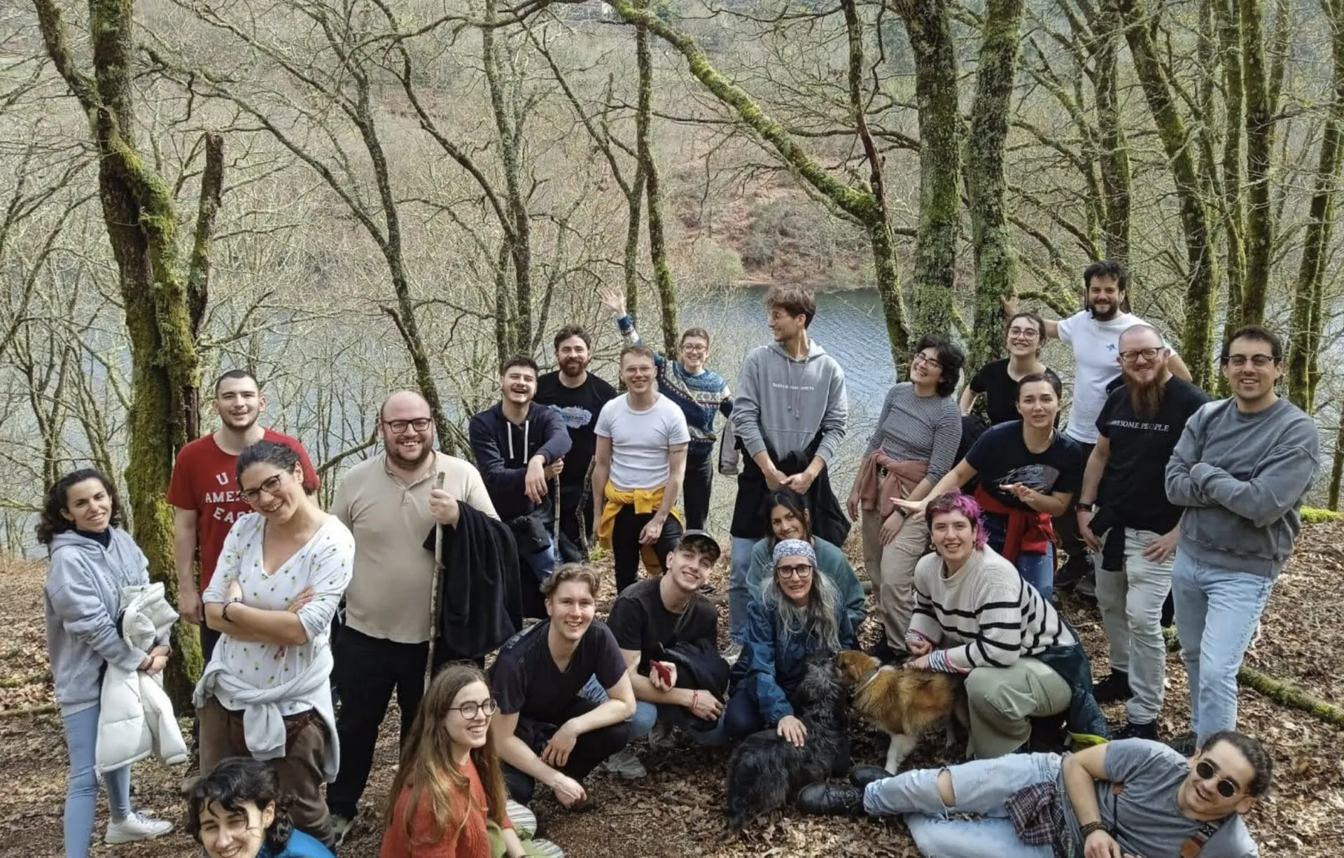 About twenty-five young people posing among mossy bare trees on a slope above a reservoir