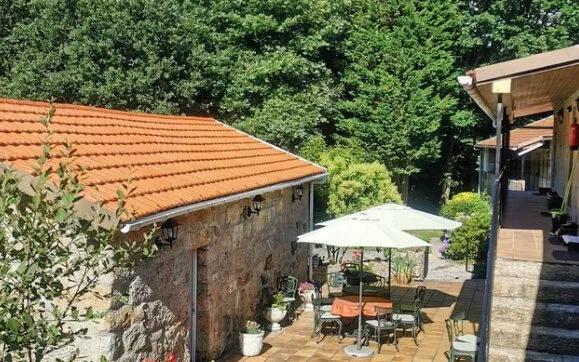 Stone building with an orange tiled roof beside a paved terrace with a white parasol and garden chairs