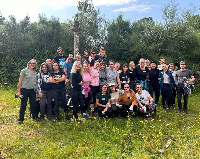 Large group of about thirty-five people posing in a meadow below a stone cross, several wearing work gloves