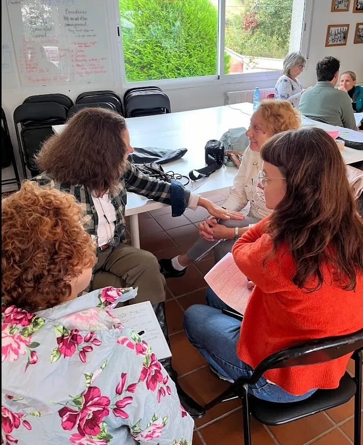 Women sitting close together in a workshop room, one reaching out to hold another’s arm, notes and a whiteboard behind