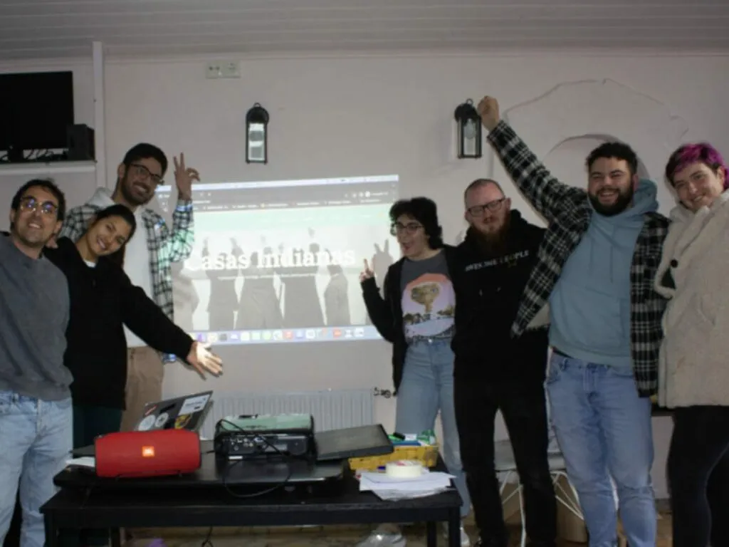Eight people cheering in front of a projected website reading ‘Casas Indianas’, with a laptop and projector on the table