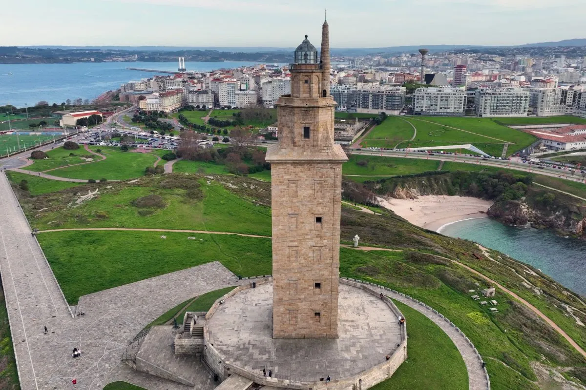 Aerial view of the Tower of Hercules lighthouse on its green headland, with A Coruña’s beaches and skyline behind