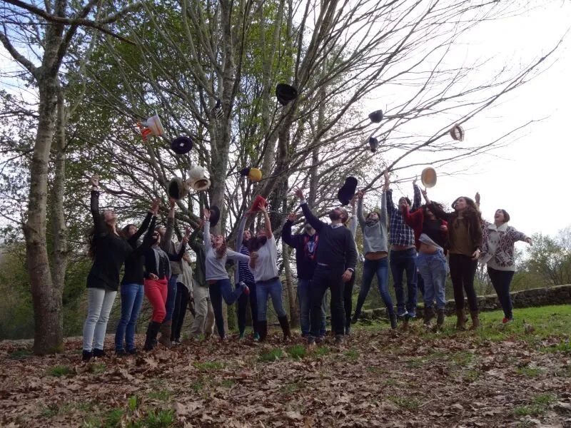 A group of people in a wood throwing their hats into the air among bare trees