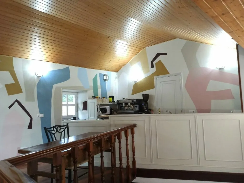 The cafe after its redesign: an abstract mural in blue, ochre and pink across the walls, with the espresso machine below it