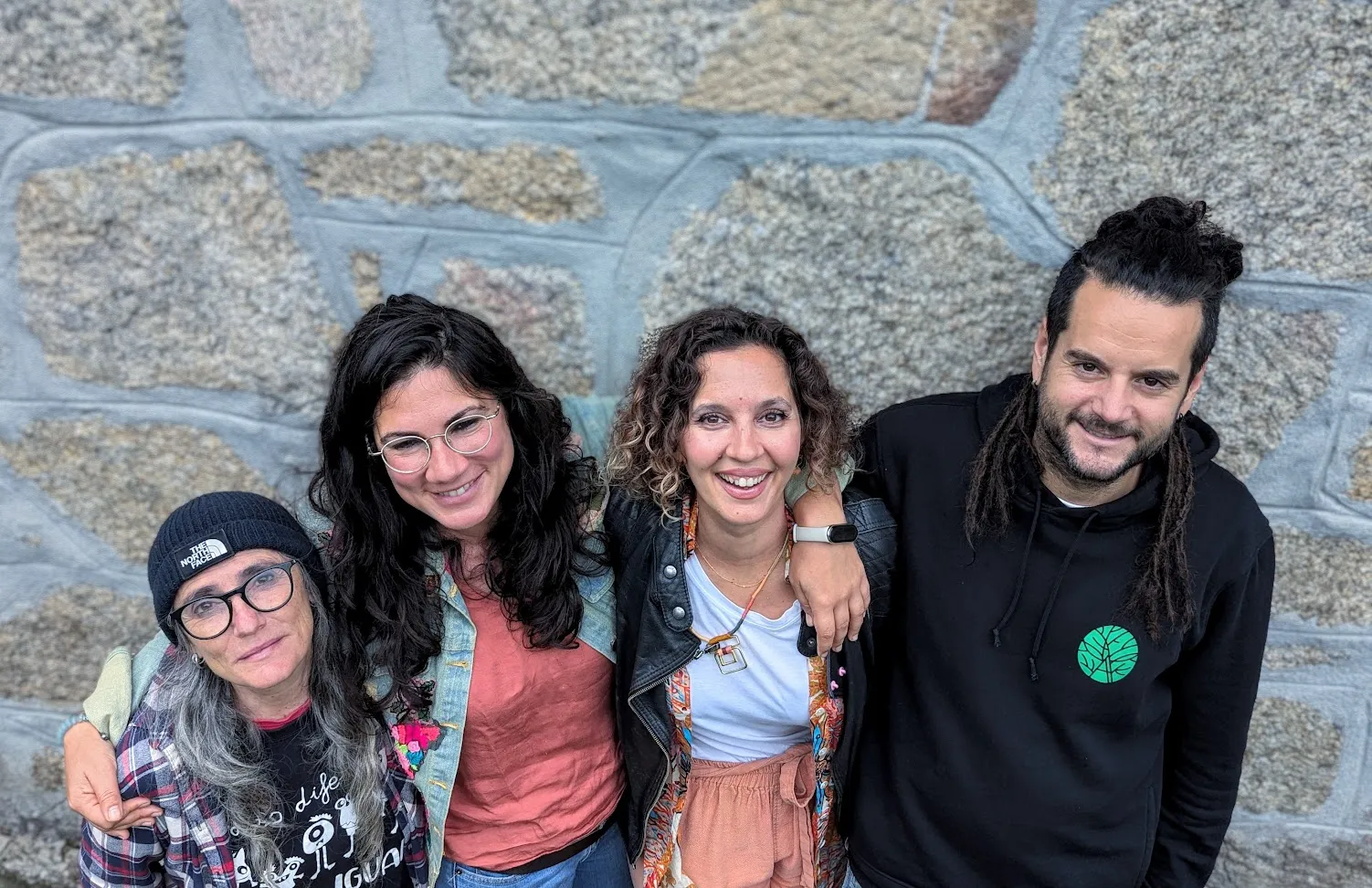 Four smiling people leaning together in front of a granite block wall