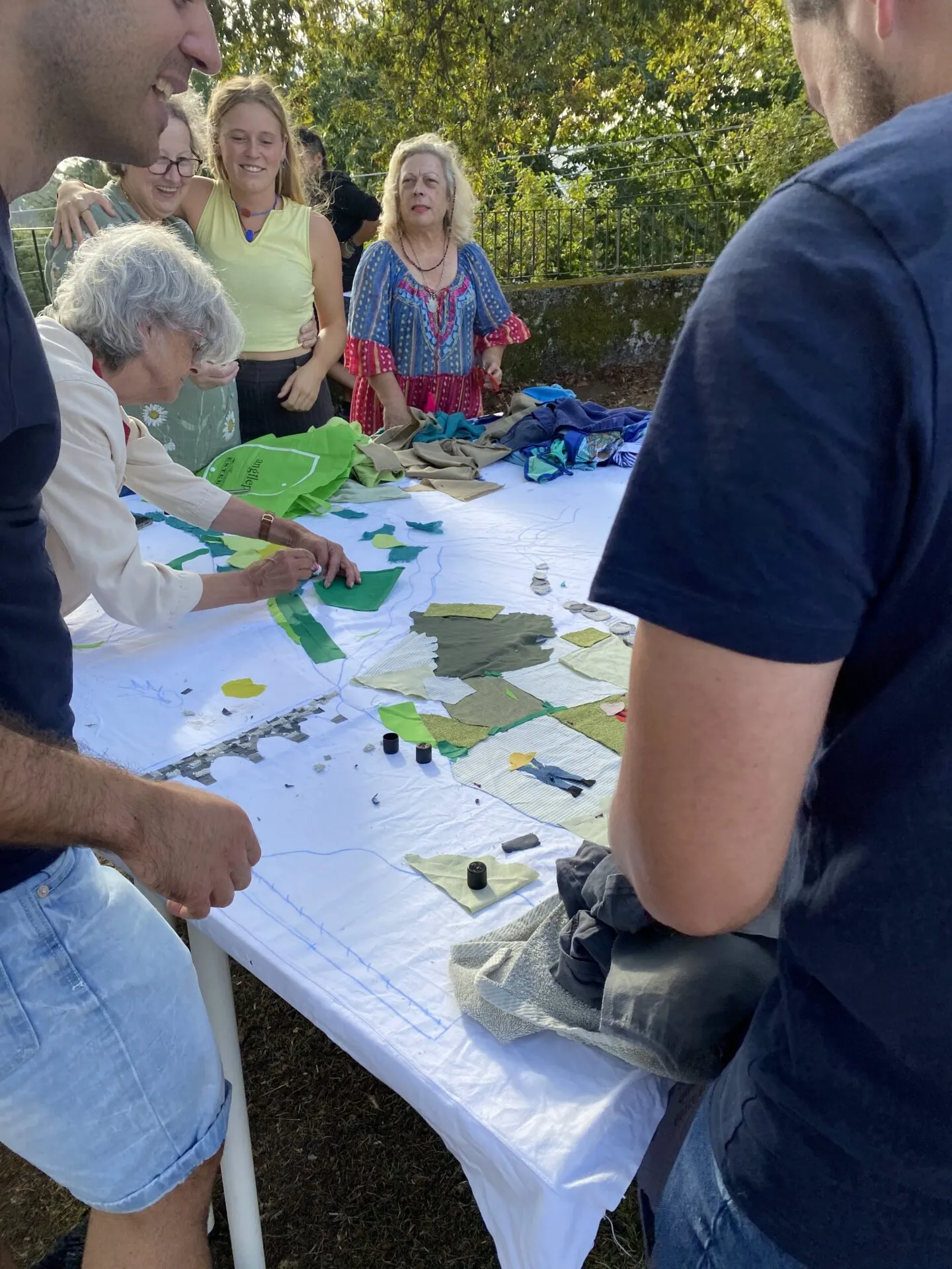 People around an outdoor table building a map out of green fabric scraps laid on a white sheet