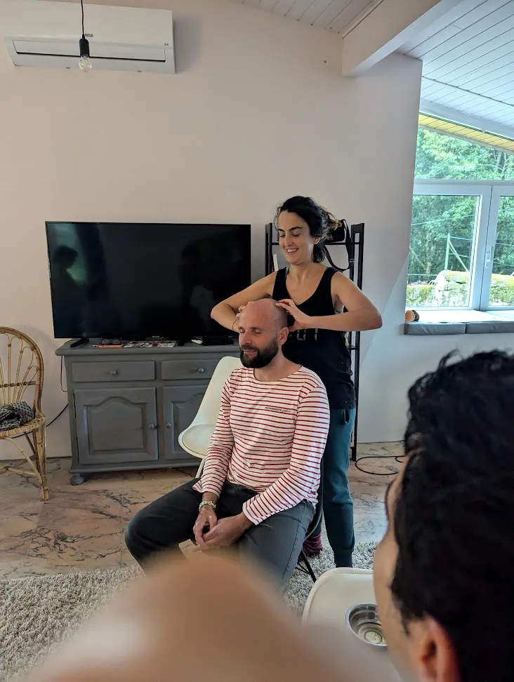 A woman giving a head massage to a seated man in the living room while others watch