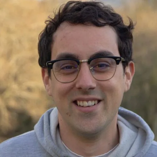 Nacho, smiling, in a grey hoodie and round glasses