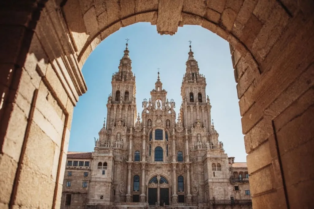 Baroque facade of Santiago de Compostela cathedral framed by a stone archway against a clear sky